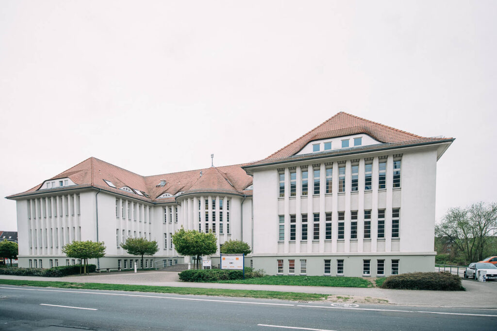 Der Standort Rostock: Ein beiges, klassizistisches Gebäude mit roten Dachziegeln und zwei Flügeln.